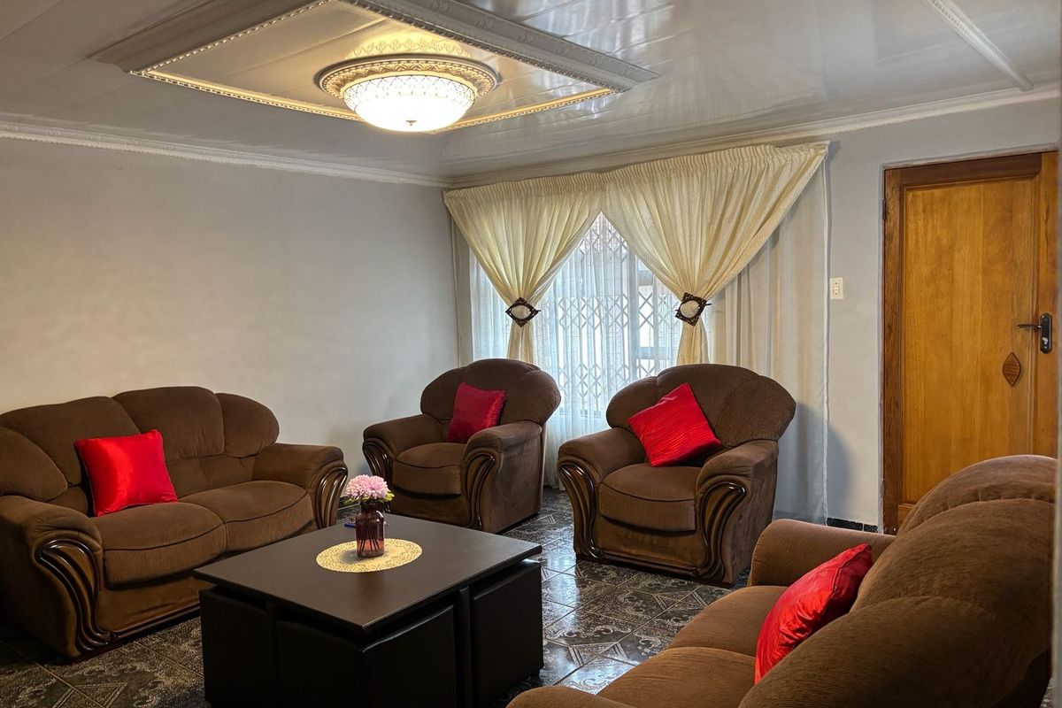 A living room featuring a coffered ceiling with central lighting, tiled flooring, and a wooden door, providing a functional and traditional living space.