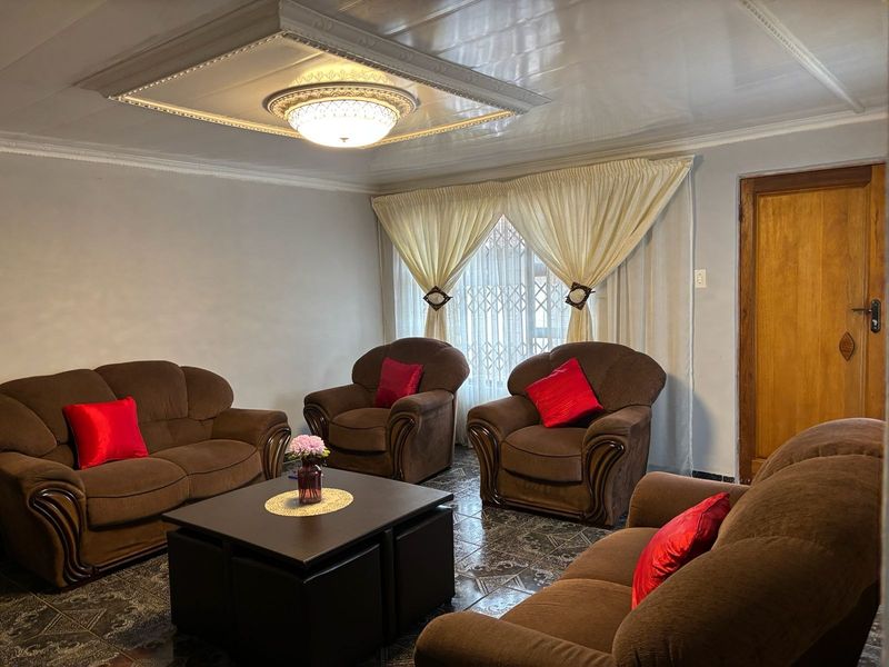 A living room featuring a coffered ceiling with central lighting, tiled flooring, and a wooden door, providing a functional and traditional living space.