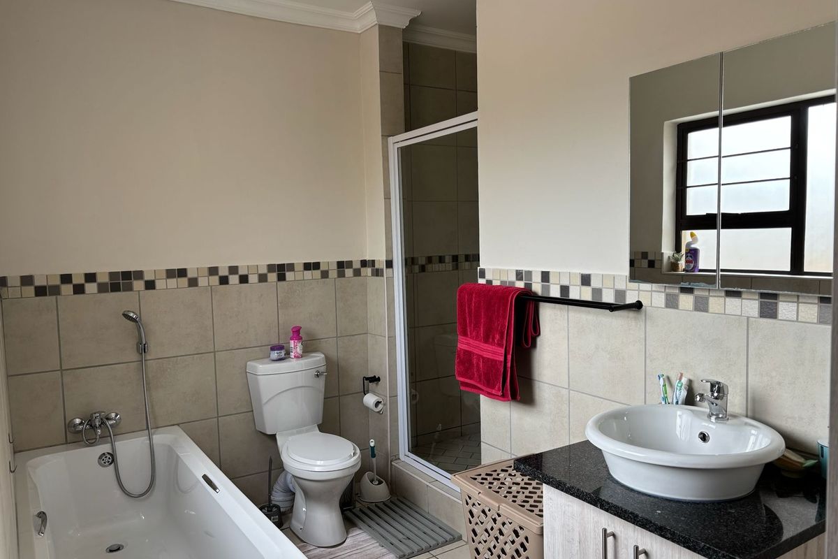 A functional bathroom featuring a bathtub, separate shower enclosure, vessel sink vanity, and neutral wall tiling with a decorative mosaic border.