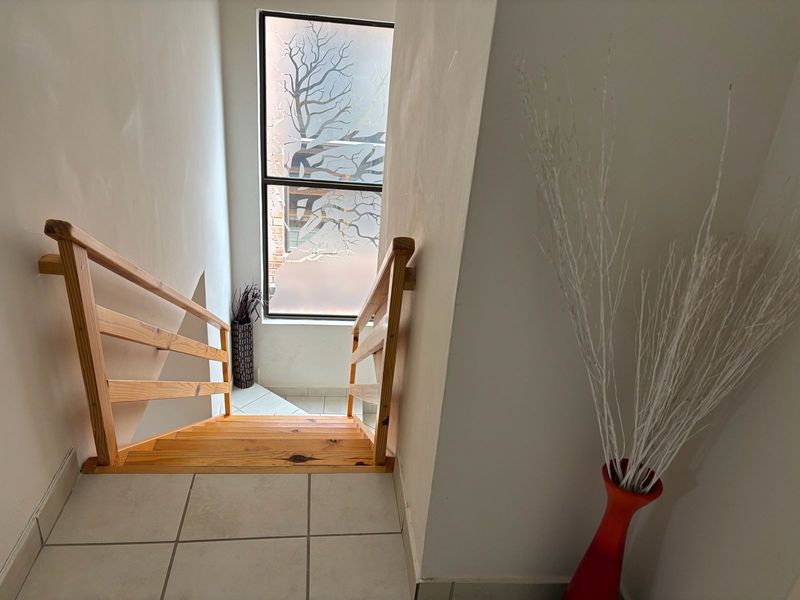 A bright hallway featuring a wooden staircase with a matching handrail, tiled flooring, and a decorative frosted window providing natural light.