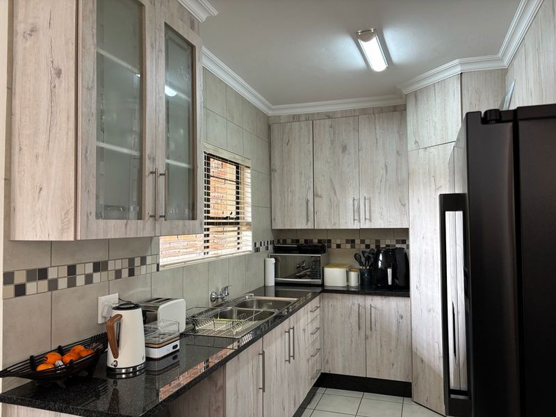 A functional kitchen featuring light wood-look laminate cabinetry, dark granite countertops, a double basin sink, and a decorative tiled backsplash.