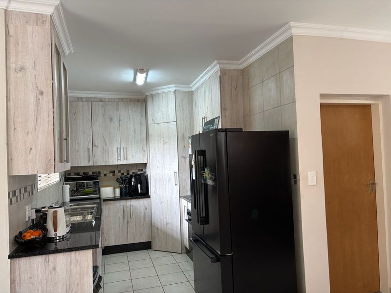 A functional kitchen featuring light wood-look laminate cabinetry, dark granite countertops, tiled backsplash, and ceramic floor tiles with classic ceiling cornices.