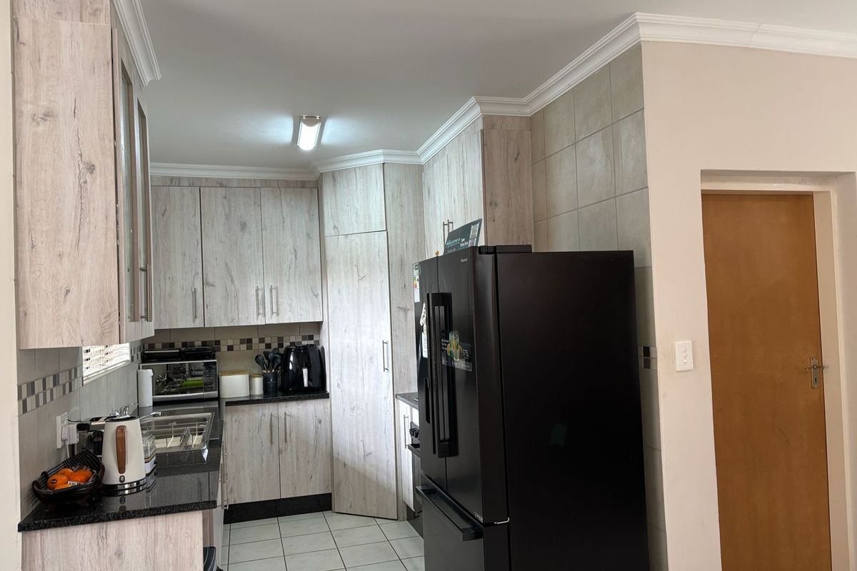 A functional kitchen featuring light wood-look laminate cabinetry, dark granite countertops, tiled backsplash, and ceramic floor tiles with classic ceiling cornices.