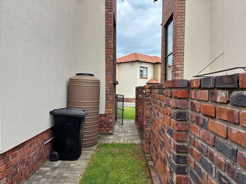 A side passage of the townhouse featuring a paved walkway, brick boundary wall, and a water storage tank.