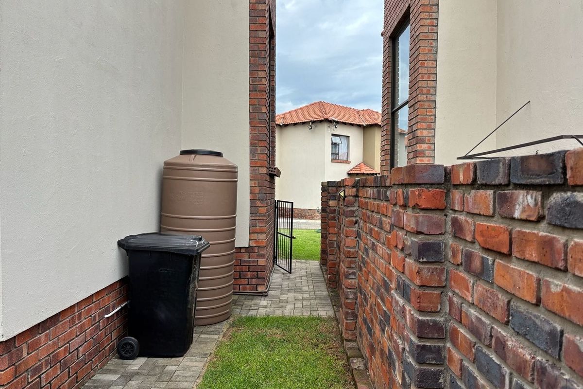 A side passage of the townhouse featuring a paved walkway, brick boundary wall, and a water storage tank.