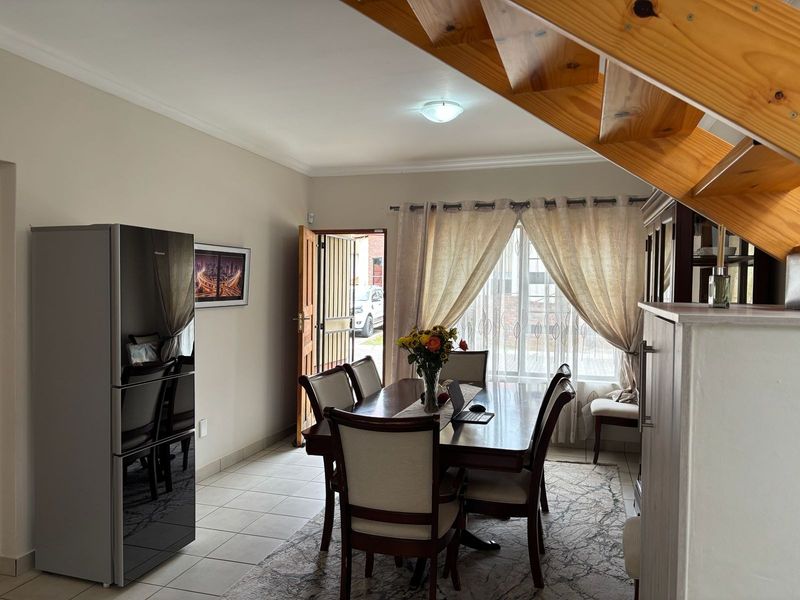 Dining area featuring tiled flooring and an open wooden staircase, with direct access to the exterior through a security gate.
