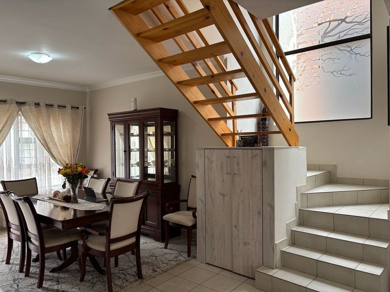 A dining area featuring a wooden staircase with built-in storage underneath, tiled flooring, and a large window providing natural light.