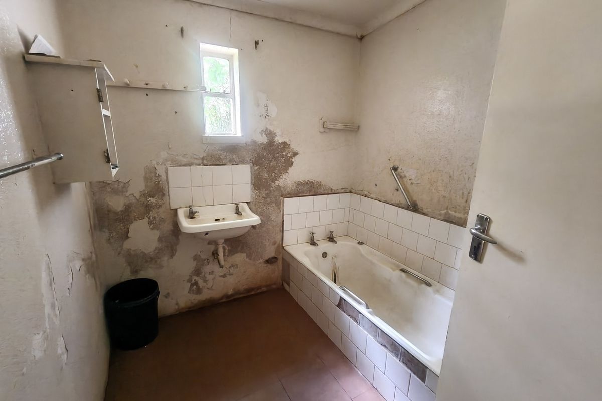 A dated bathroom requiring significant renovation, featuring a built-in bathtub and wall-mounted basin with visible wall surface deterioration.