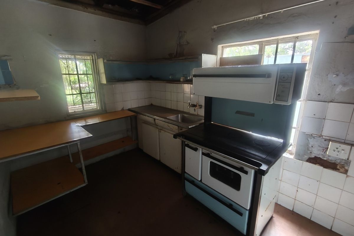 A dilapidated kitchen space featuring a vintage stove, stainless steel sink, and tiled splashbacks, requiring significant renovation and structural repairs.