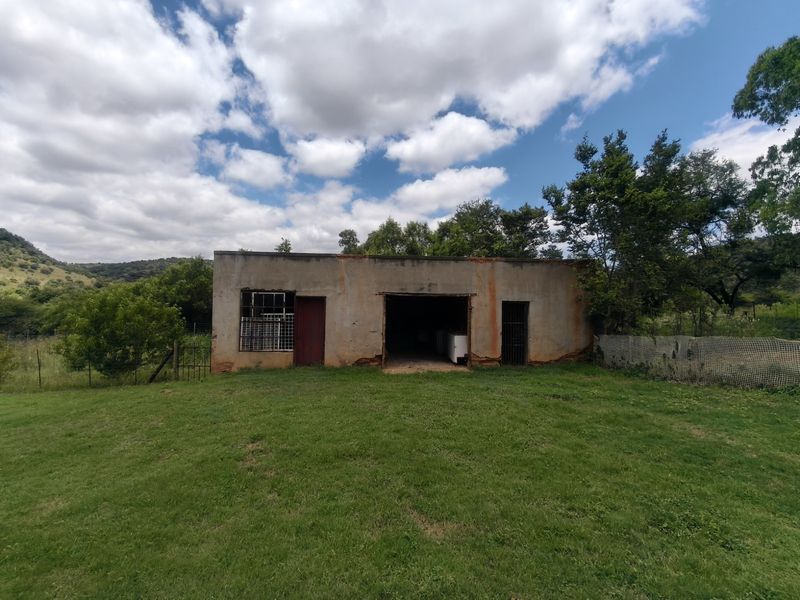 A weathered outbuilding on a farm property featuring a large open bay, metal security gates, and steel window frames set in a rural landscape.