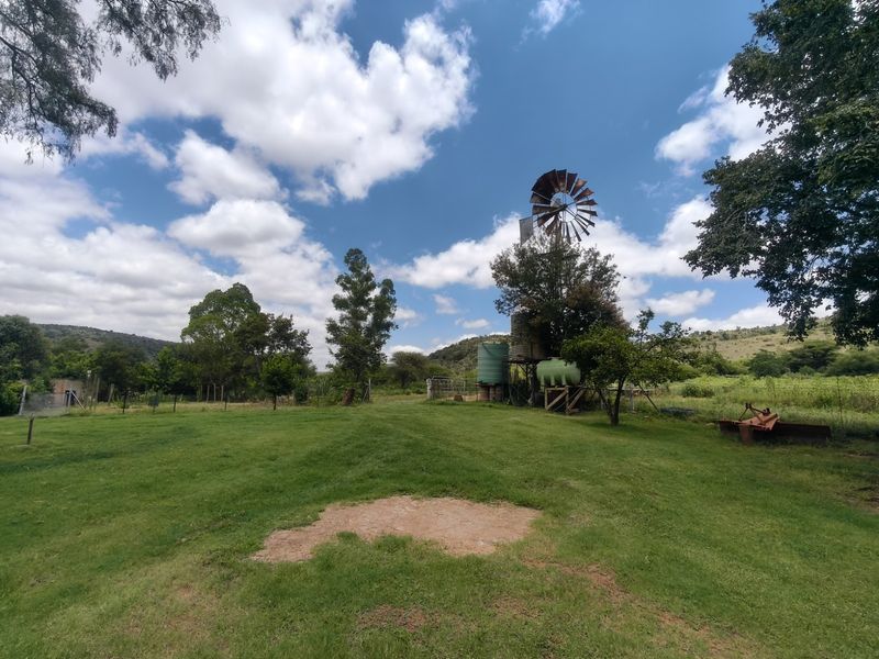 A spacious farm garden featuring a traditional windmill and water storage tanks set against a scenic rural landscape.