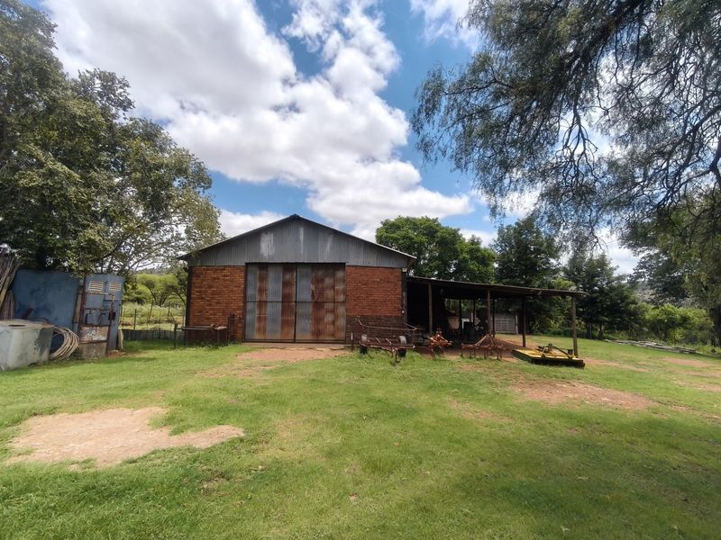 A rustic brick farm barn featuring large corrugated metal sliding doors and an attached covered lean-to area, set within a spacious rural landscape.