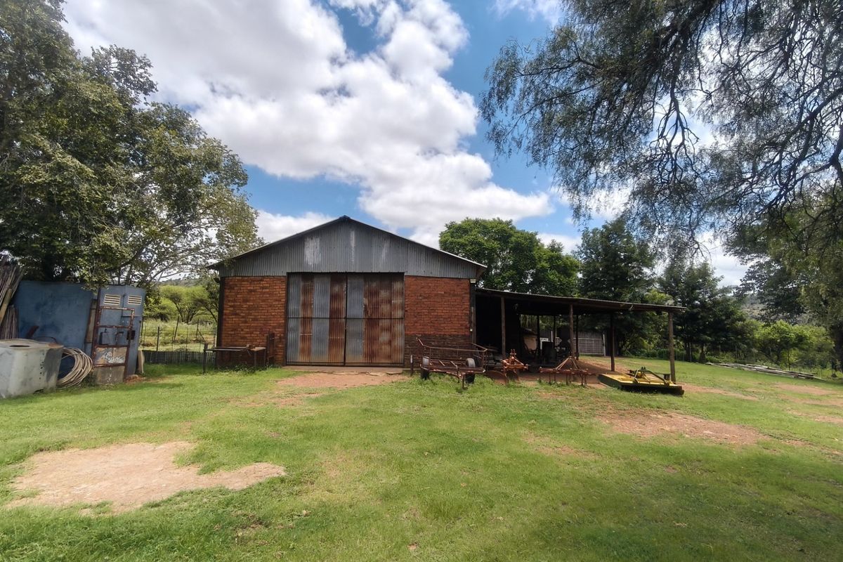 A rustic brick farm barn featuring large corrugated metal sliding doors and an attached covered lean-to area, set within a spacious rural landscape.