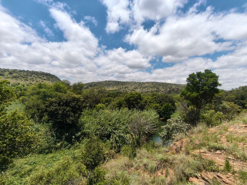 A scenic landscape view overlooking a lush green valley with a river and rolling hills under a cloudy blue sky.