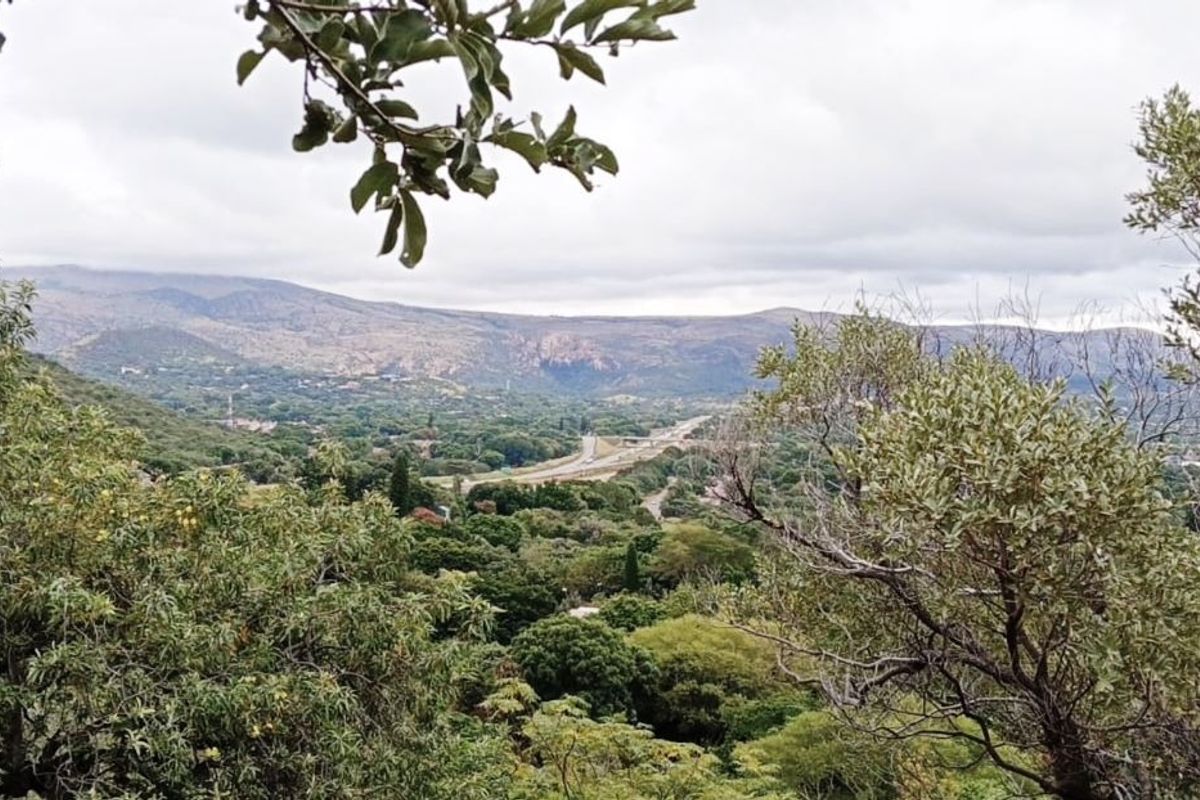 A scenic elevated view overlooking a lush green valley with distant mountains and a road winding through the landscape.