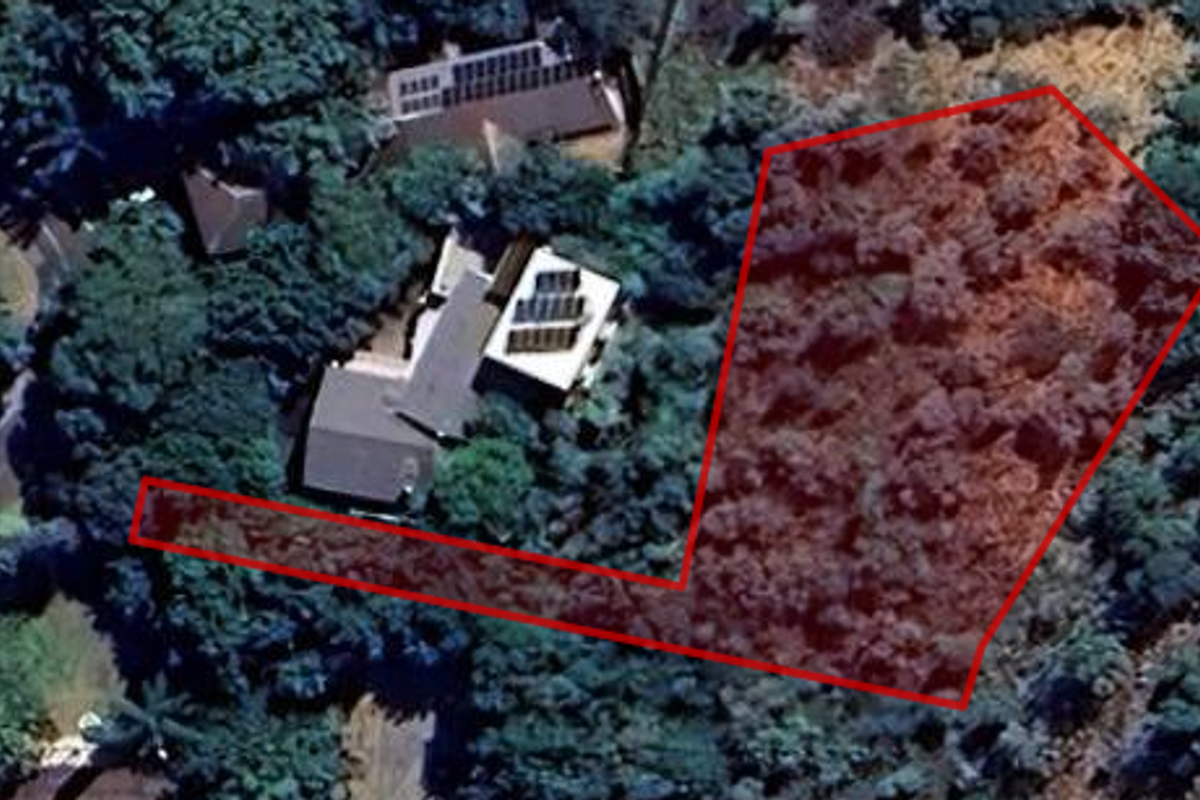 An aerial view of a residential vacant land plot outlined in red, featuring dense vegetation and surrounding trees.