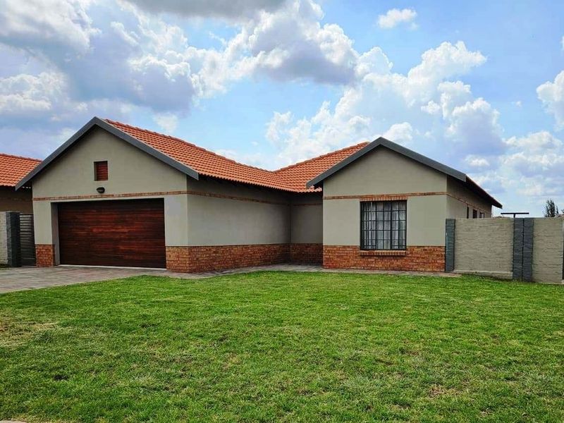 A well-maintained single-story house featuring a tiled roof, brick accents, a wooden garage door, and a neat front lawn.