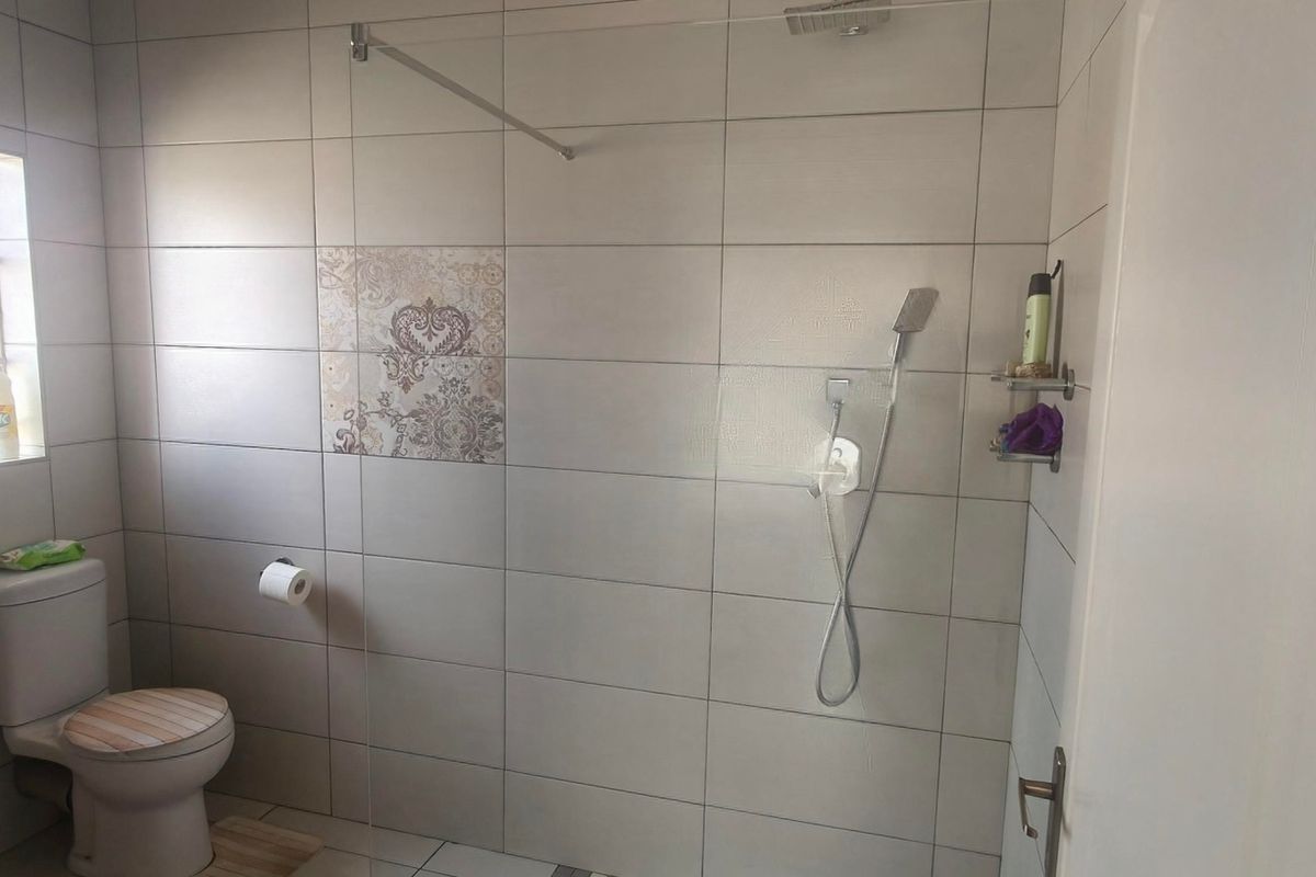 A modern bathroom featuring a walk-in shower with a glass screen, handheld shower attachment, and neutral ceramic wall tiling.