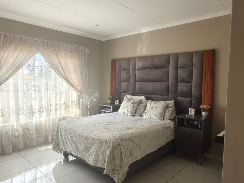 A well-maintained bedroom featuring tiled flooring, a large upholstered headboard, and natural light through a window with sheer curtains.