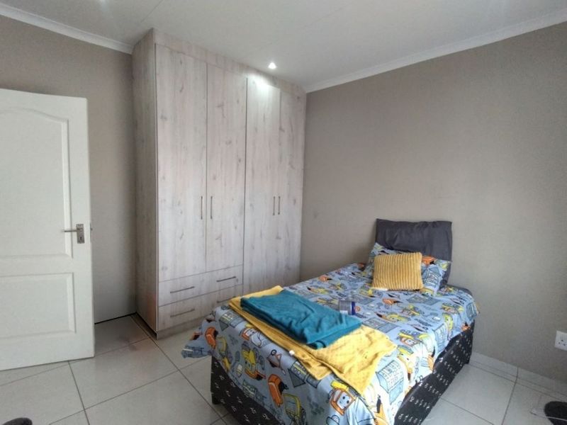 A well-maintained bedroom featuring neutral wall tones, light wood-grain built-in wardrobes, and clean tiled flooring.
