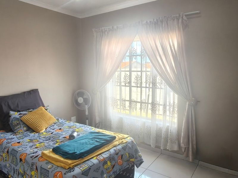 A functional bedroom featuring tiled flooring and a window fitted with security bars, providing natural light and basic security.