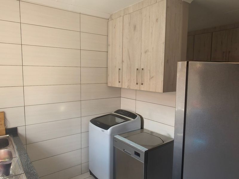 A functional laundry area featuring modern light wood cabinetry, tiled walls, a stainless steel sink, and dedicated space for laundry appliances.