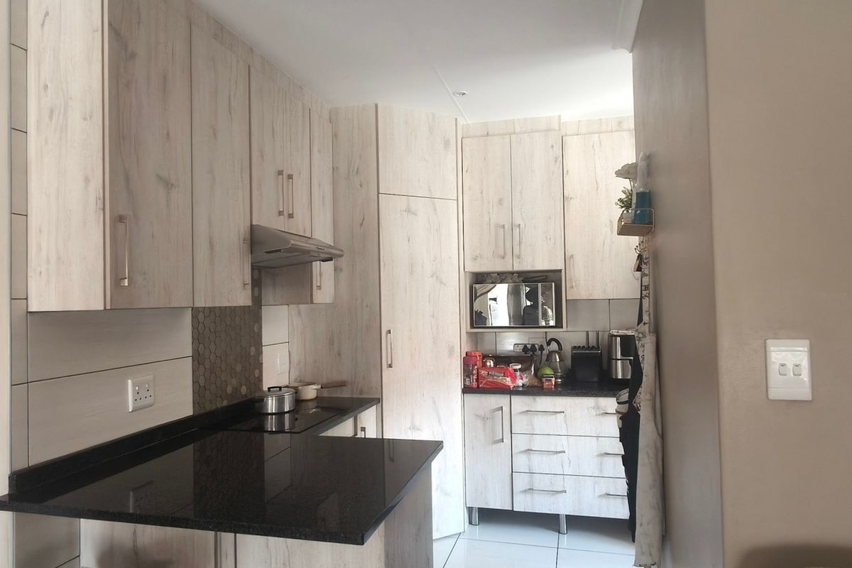 A functional kitchen featuring light wood-grain cabinetry, dark granite countertops, a built-in hob, and an extractor fan with a modern tiled backsplash.