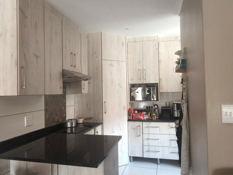 A functional kitchen featuring light wood-grain cabinetry, dark granite countertops, a built-in hob, and an extractor fan with a modern tiled backsplash.