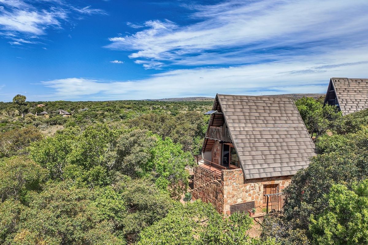 Aerial view of an A-frame house featuring stone masonry walls and a tiled roof, nestled within a lush, natural bushveld landscape.