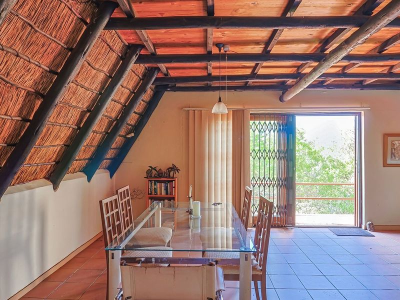 Dining area featuring a rustic thatched roof with exposed timber rafters, tiled flooring, and direct access to an outdoor balcony through sliding glass doors.