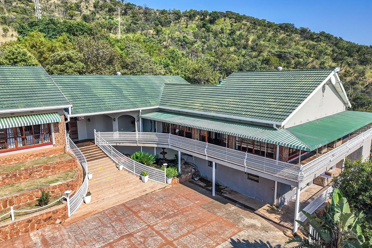 Aerial view of the rear elevation featuring a large paved courtyard, stone retaining walls, and a spacious balcony with wrought iron railings.