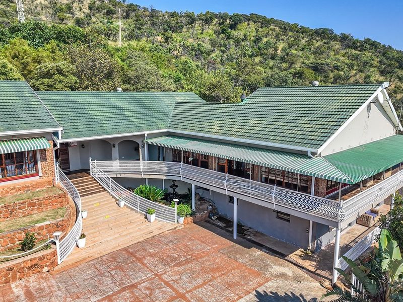 Aerial view of the rear elevation featuring a large paved courtyard, stone retaining walls, and a spacious balcony with wrought iron railings.