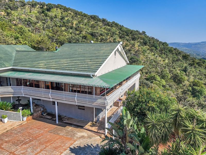Elevated rear view of the farmhouse featuring a spacious covered veranda, tiled roof, and expansive views over the surrounding natural landscape.