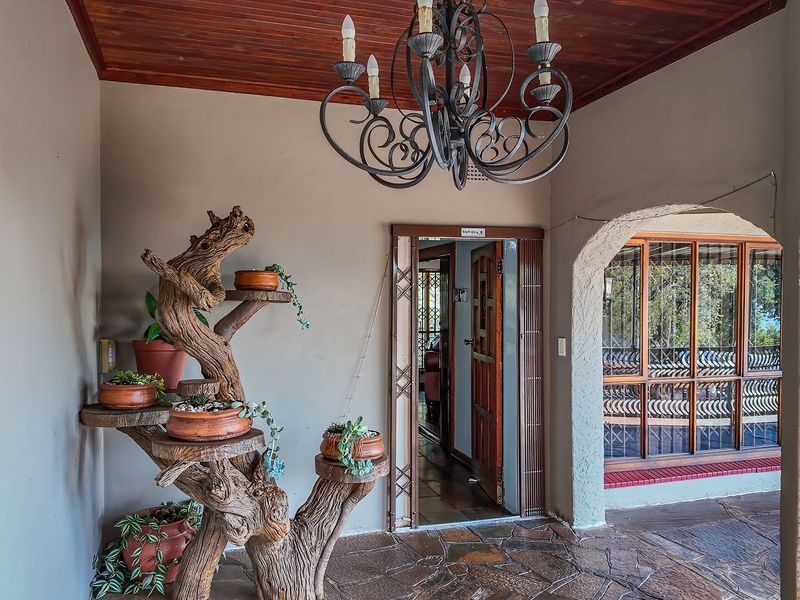 A covered patio area featuring stone flooring, a timber ceiling, and a decorative wrought iron chandelier, providing a charming entrance to the home.