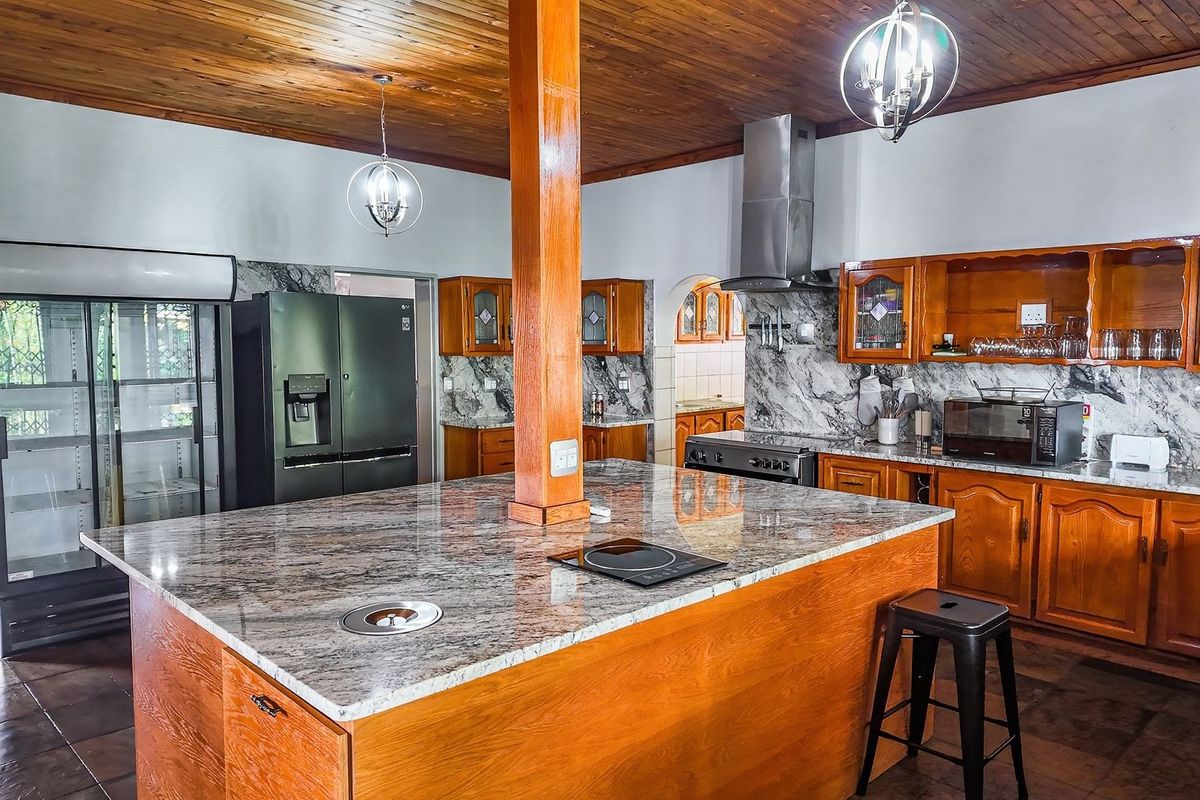 Spacious kitchen featuring warm wooden cabinetry, granite countertops, a central island with integrated cooktop, and a distinctive wooden ceiling.