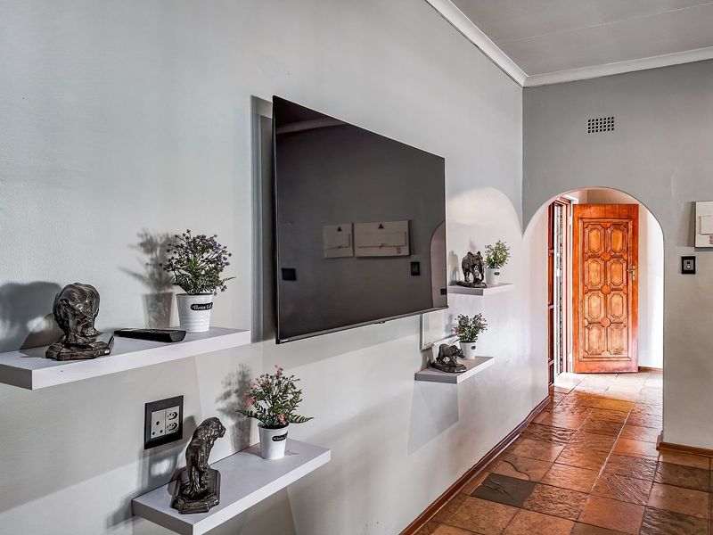 A well-maintained hallway featuring tiled flooring, an arched entryway, and wall-mounted shelving, leading towards a solid wood entrance door.