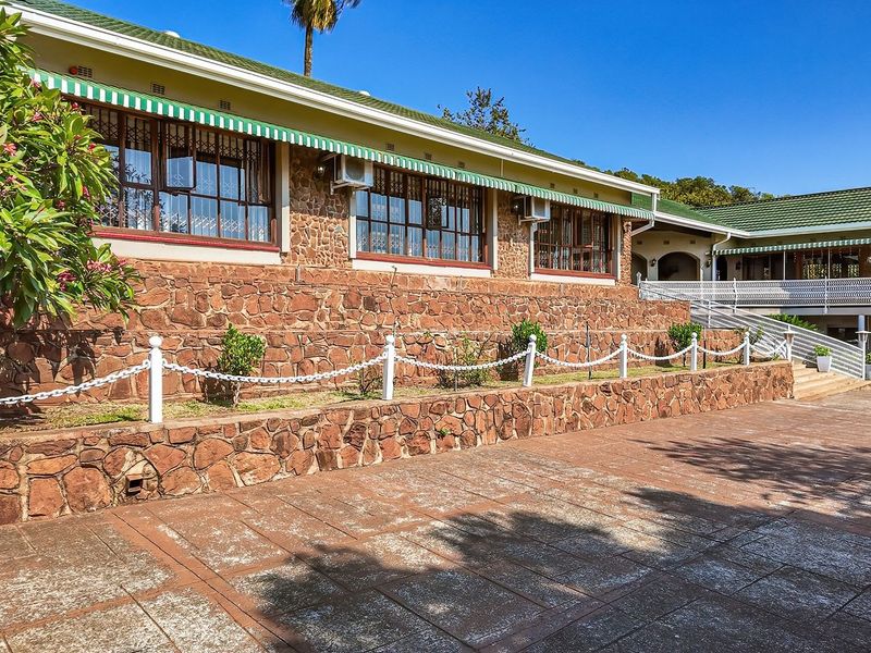 Rear elevation of the farm property featuring stone cladding, a tiled roof, and a spacious paved patio area with retaining walls.