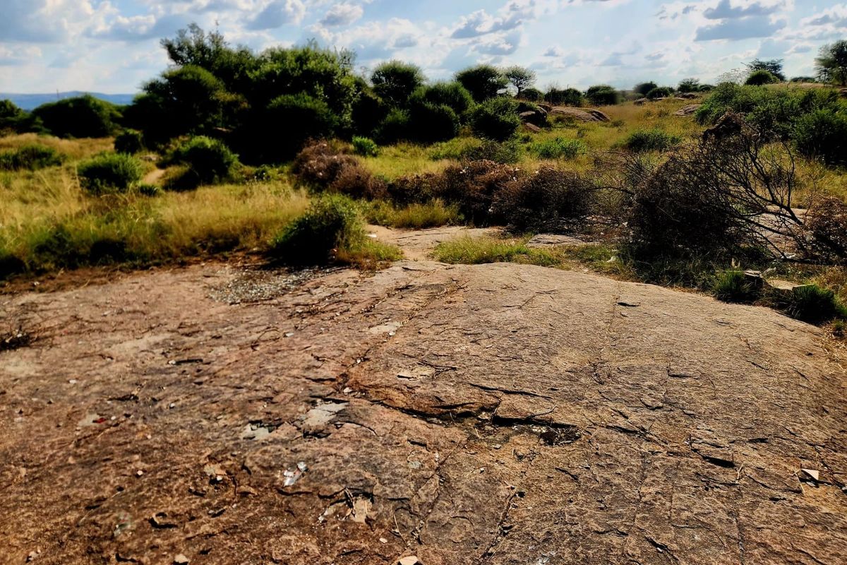 A view of a vacant residential plot featuring natural rock formations and indigenous vegetation under a partly cloudy sky.