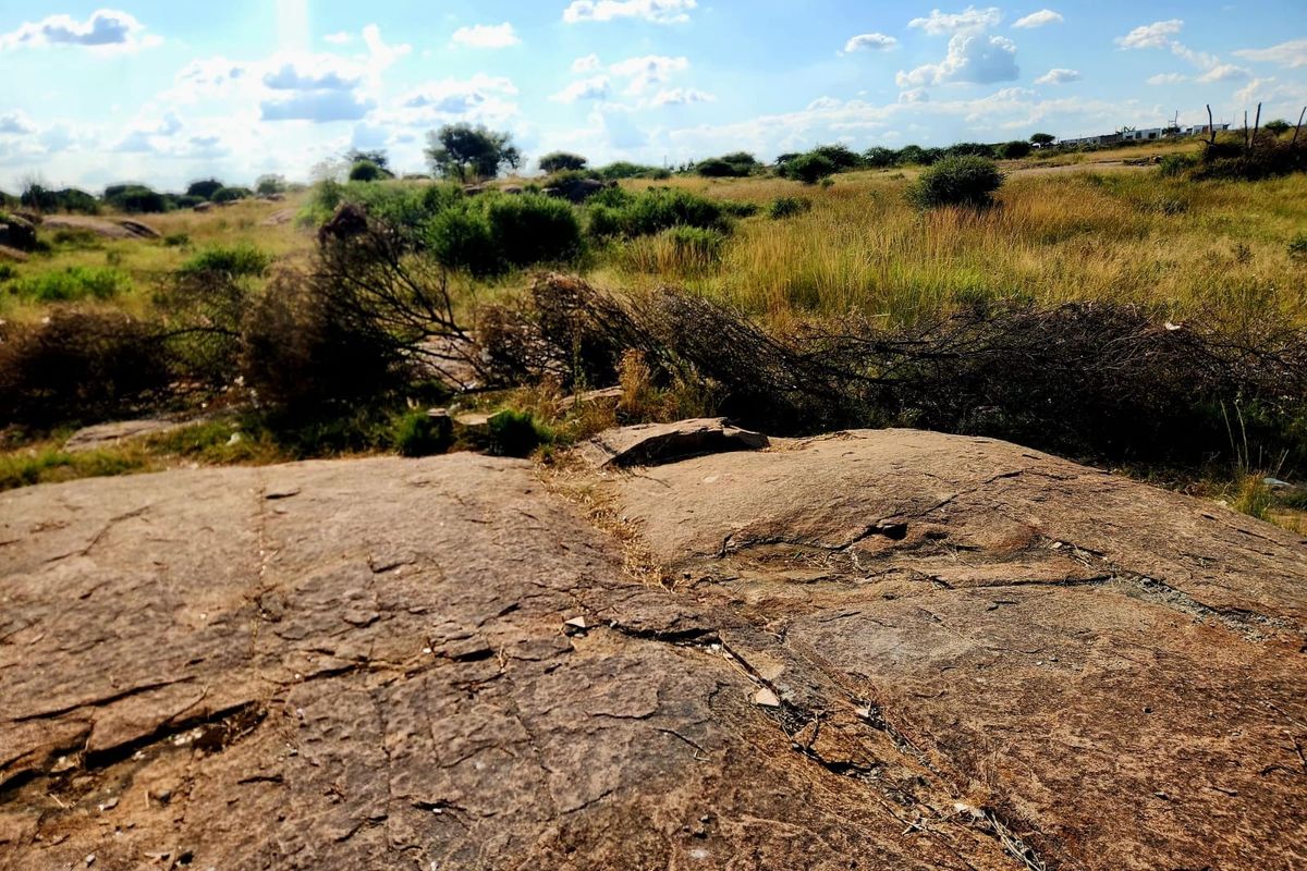 A view of undeveloped residential land featuring natural rock formations and native vegetation under a clear sky.