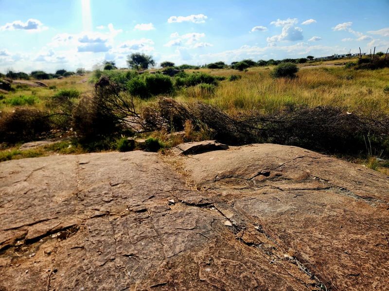 A view of undeveloped residential land featuring natural rock formations and native vegetation under a clear sky.