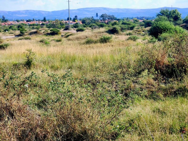 A view of the vacant residential land featuring natural grass and shrubbery with a distant view of the surrounding neighborhood and mountains.