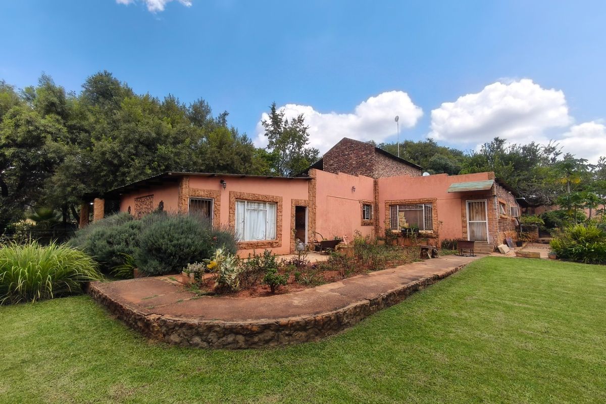 Rear view of a farm-style residence featuring plastered masonry walls, stone-clad accents, and a well-maintained lawn with a stone retaining wall.