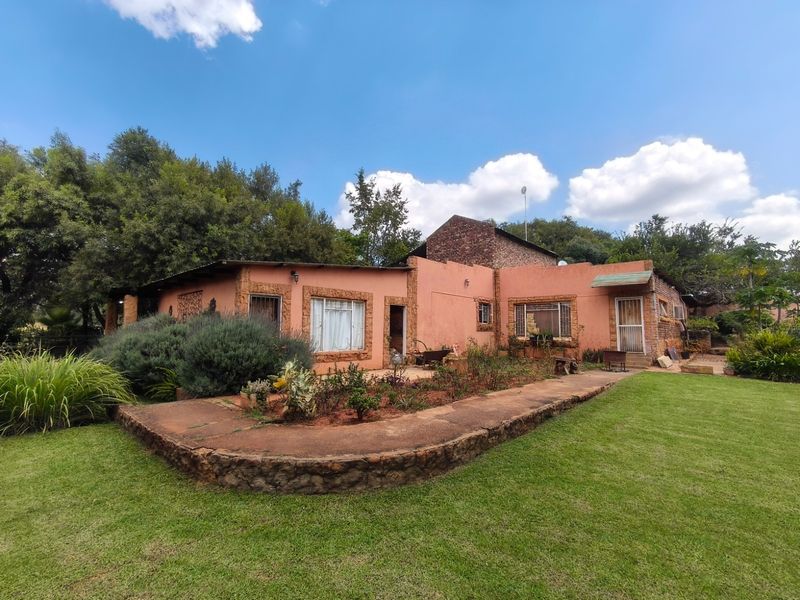 Rear view of a farm-style residence featuring plastered masonry walls, stone-clad accents, and a well-maintained lawn with a stone retaining wall.