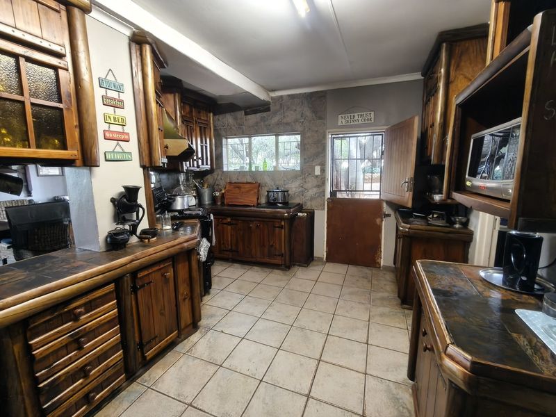 Rustic farm-style kitchen featuring extensive wooden cabinetry, tiled countertops, and a traditional stable door, offering a functional layout with potential for modernization.