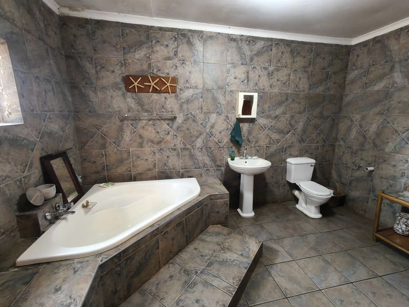 A spacious bathroom featuring a corner bathtub, pedestal sink, and toilet, finished with full-height stone-look wall tiles and matching floor tiles.