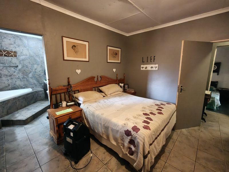 A bedroom featuring tiled flooring and an open-plan en-suite bathroom with a built-in bathtub and stone-tiled wall finishes.