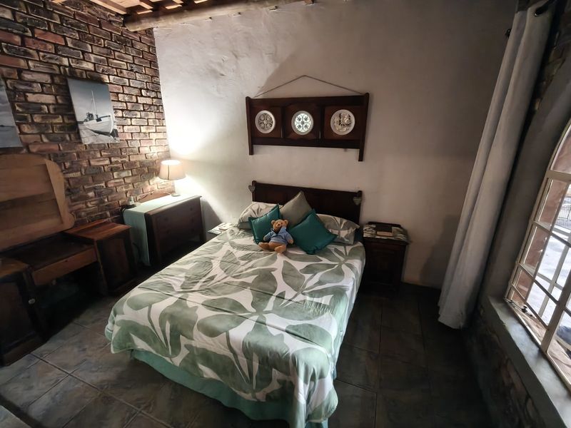 A rustic bedroom featuring exposed brick walls, timber ceiling beams, and tiled flooring, offering a cozy and character-filled living space.