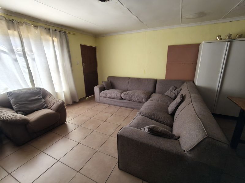 A living room featuring tiled flooring and ceiling panels, currently requiring cosmetic updates to the walls and ceiling to improve its overall condition.