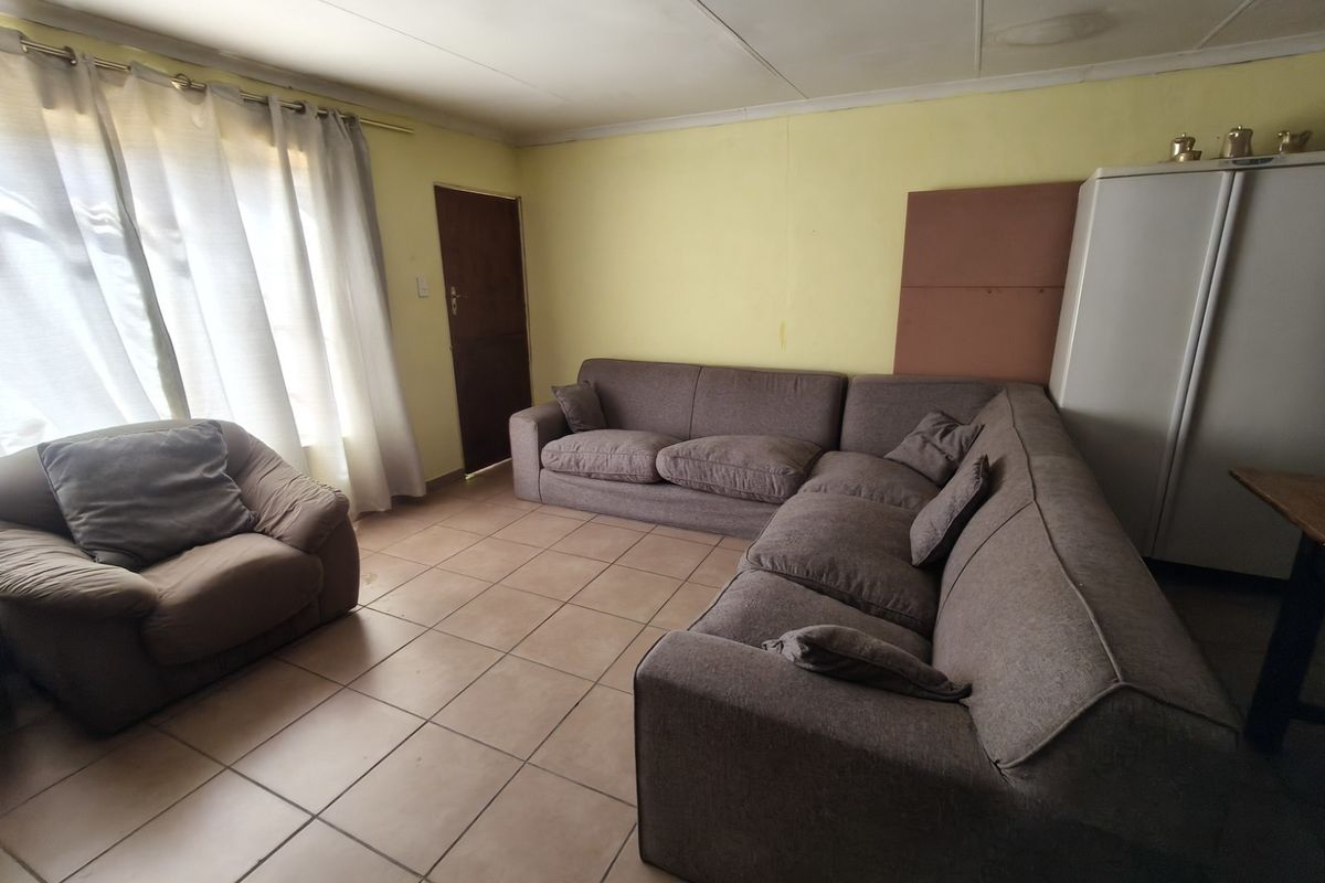 A living room featuring tiled flooring and ceiling panels, currently requiring cosmetic updates to the walls and ceiling to improve its overall condition.