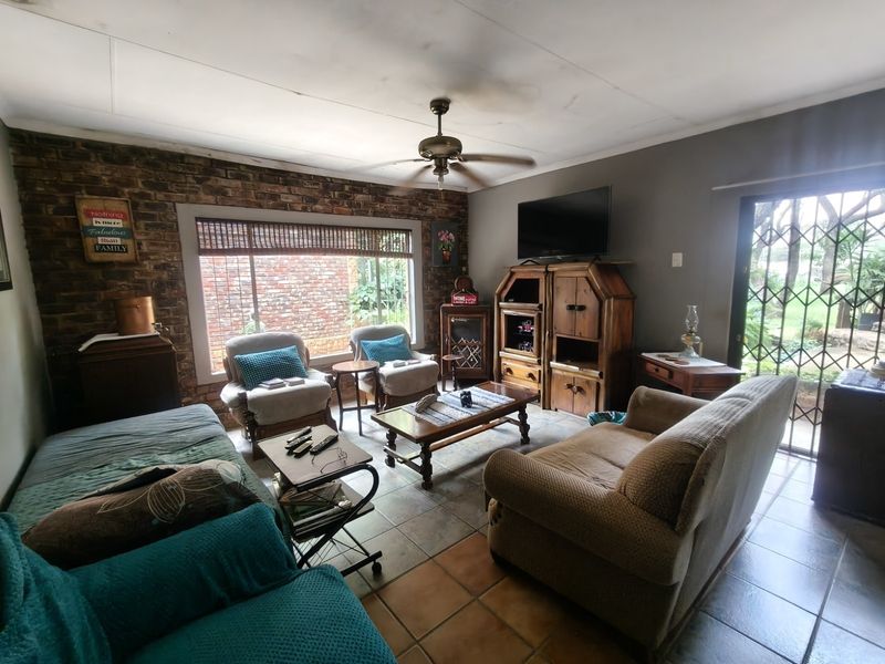 A living room featuring an exposed brick feature wall, tiled flooring, and a ceiling fan, with direct access to the garden through a security gate.